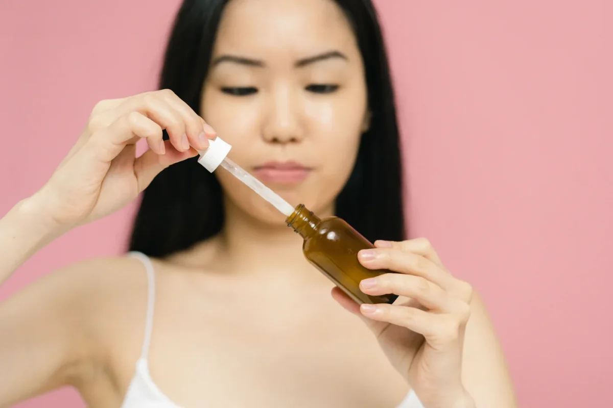 Tay cầm chai serum và ống nhỏ giọt trên nền hồng