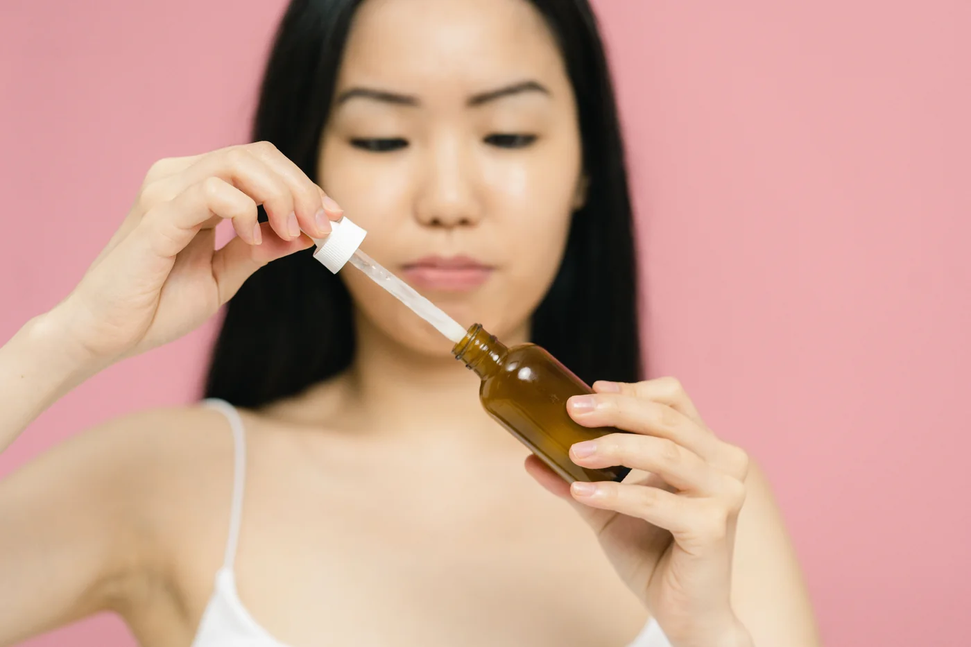 Tay cầm chai serum và ống nhỏ giọt trên nền hồng